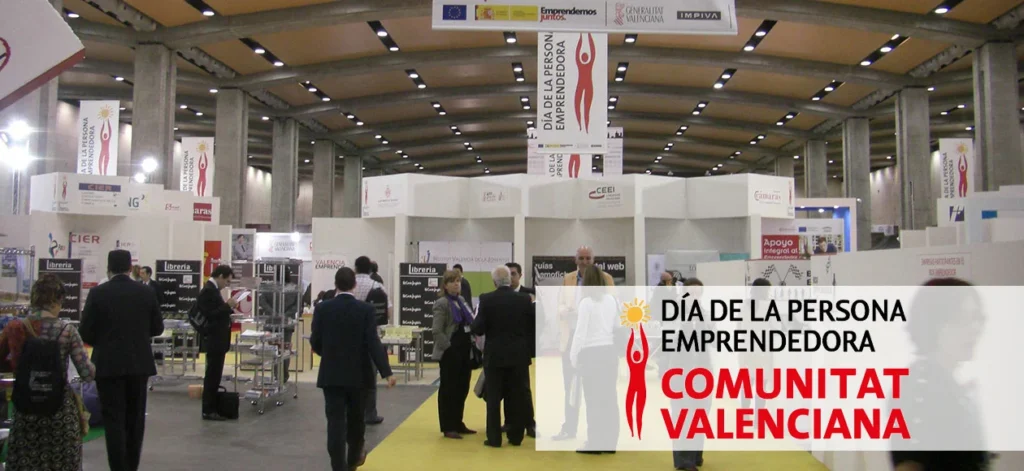 An entrepreneurial fair in Valencia, Spain, with booths and people networking, celebrating the Day of the Entrepreneur in the Valencian Community.