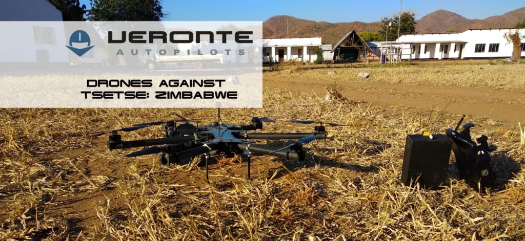 The image features a drone positioned in a dry, harvested field, with a remote control and another electronic device beside it.