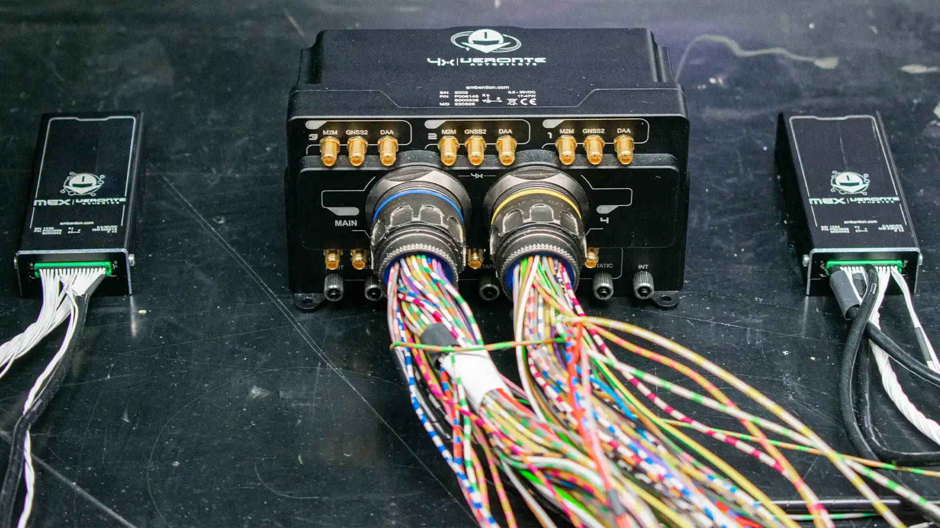The image displays a setup of Embention's "MEX | Veronte Avionics" and "4x | Veronte Autopilots" modules connected by multicolored wires, indicating a testing or integration scenario.